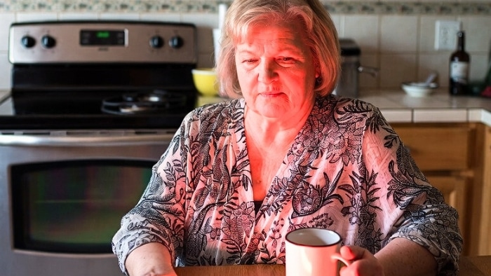 mature woman sitting at the table and sipping hot cup of coffee whle enjoing dry skin in winter remedies: red light therapy and learning - how to take care of skin in winter naturally